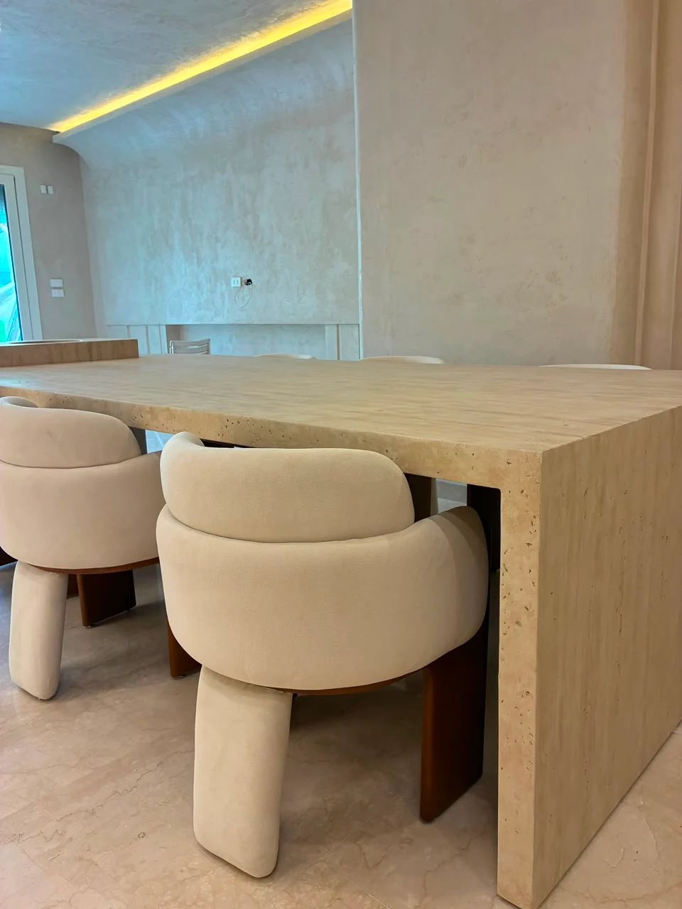 A travertine dining table with cream upholstered dining chairs in a finished room