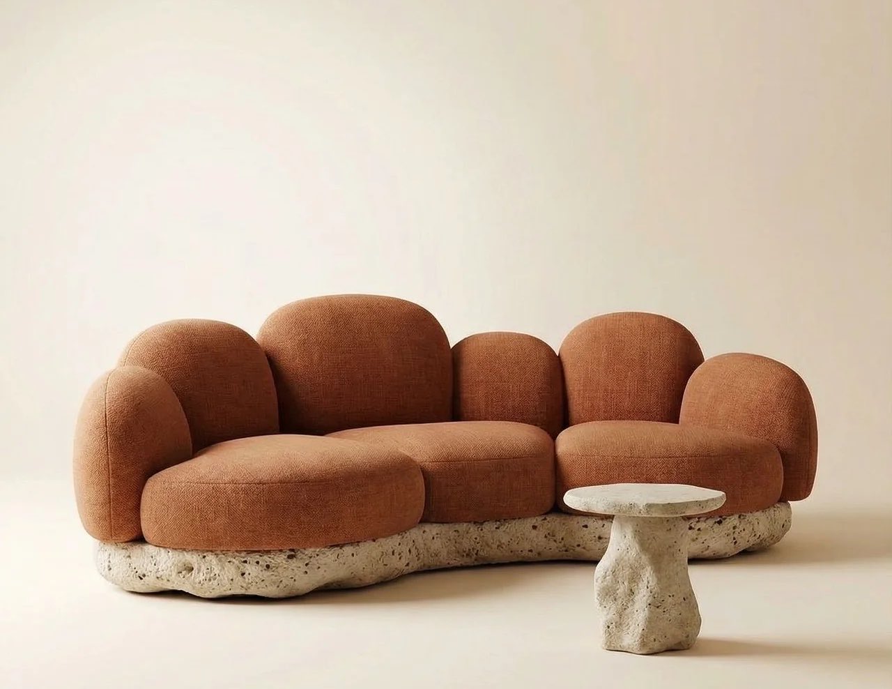 A rust bouclé Attik sofa on a rough stone base beside a small stone side table